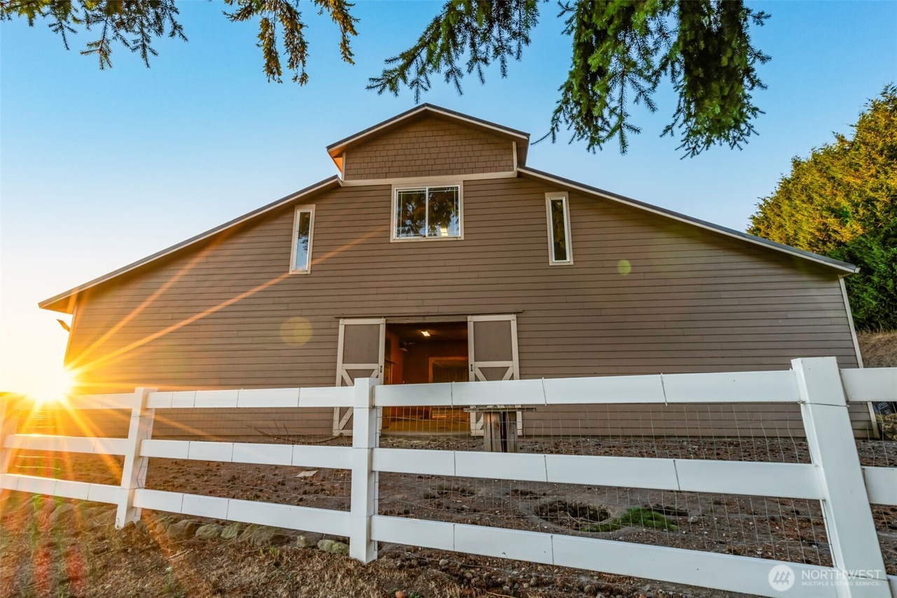 Equestrian barn with white fencing at sunset